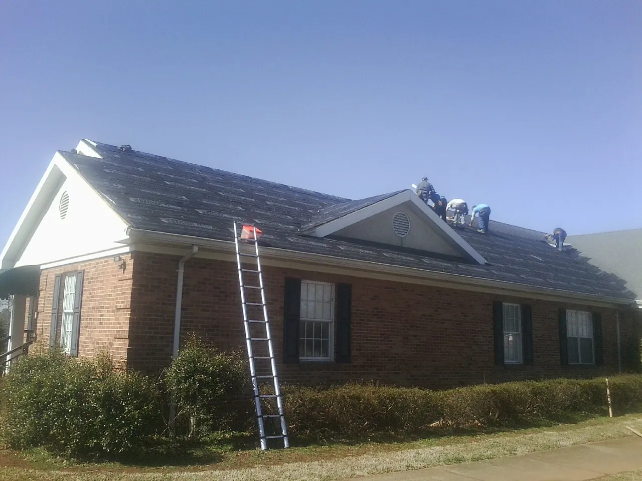 Crew tearing shingles off a brick ranch roof with a ladder set — Emergency Roof Repair work by our crew in Peachtree City