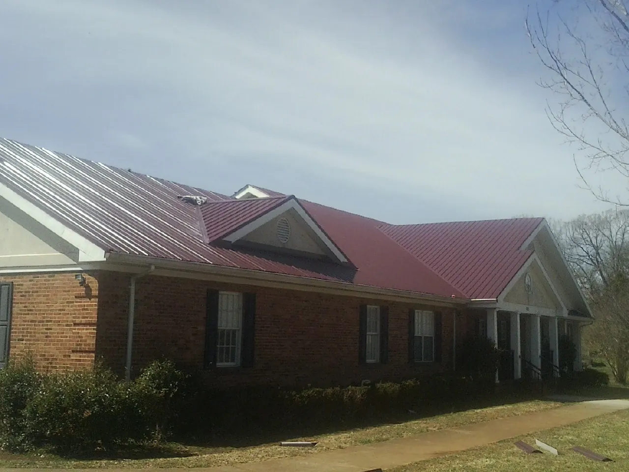 Red metal roof with gabled entries on a long brick building, from a Hail Damage Roof Repair job in Peachtree City