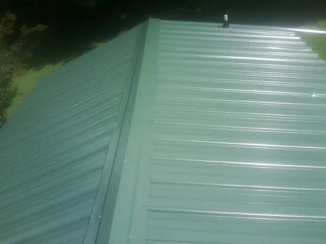 New green metal panels meeting at the ridge of a roof — Flat Roof Repair work by our crew in Peachtree City