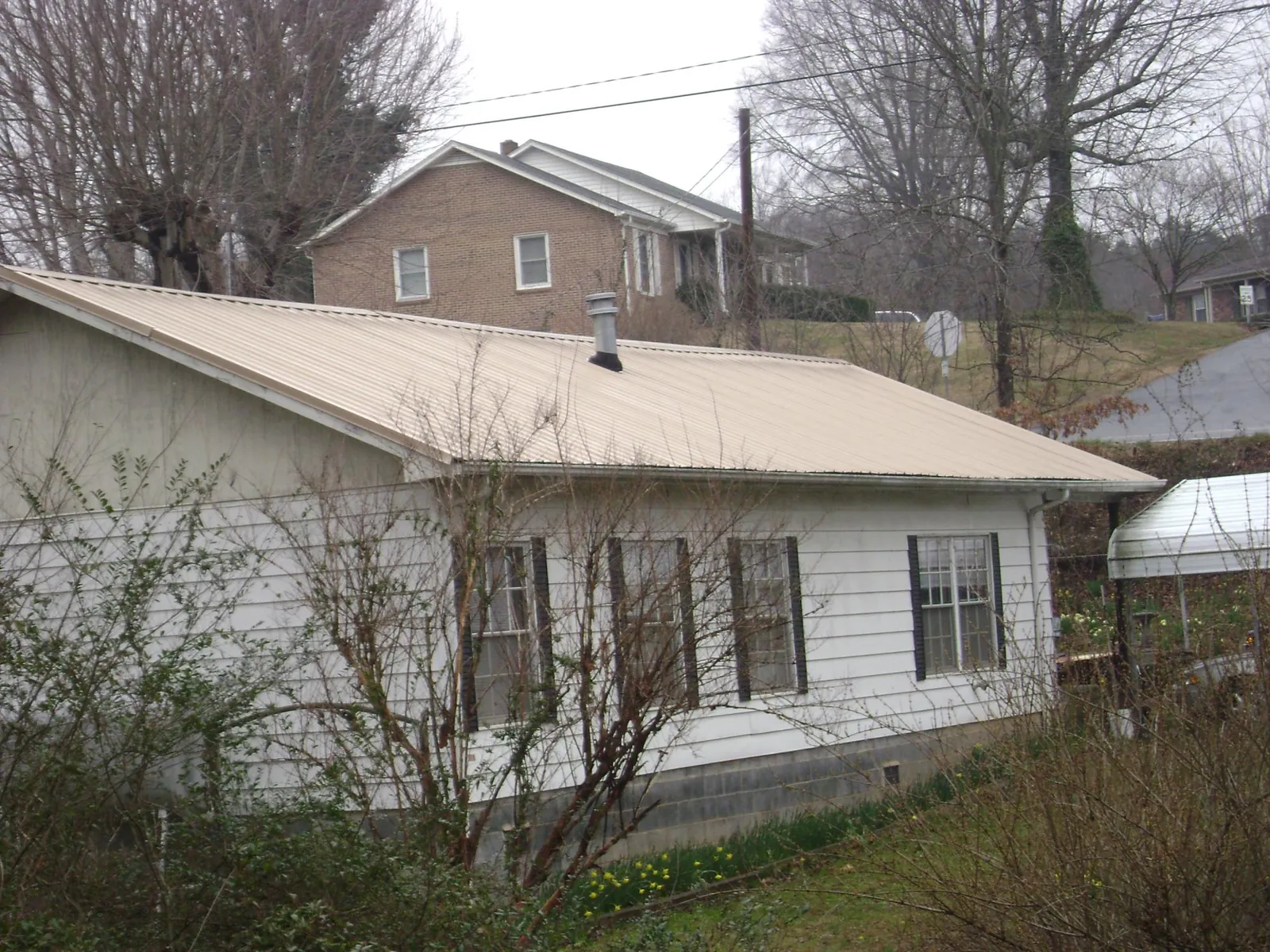 Tan metal roof on a white sided house set into a hillside — Commercial Roofing by Roofing Brothers in Peachtree City